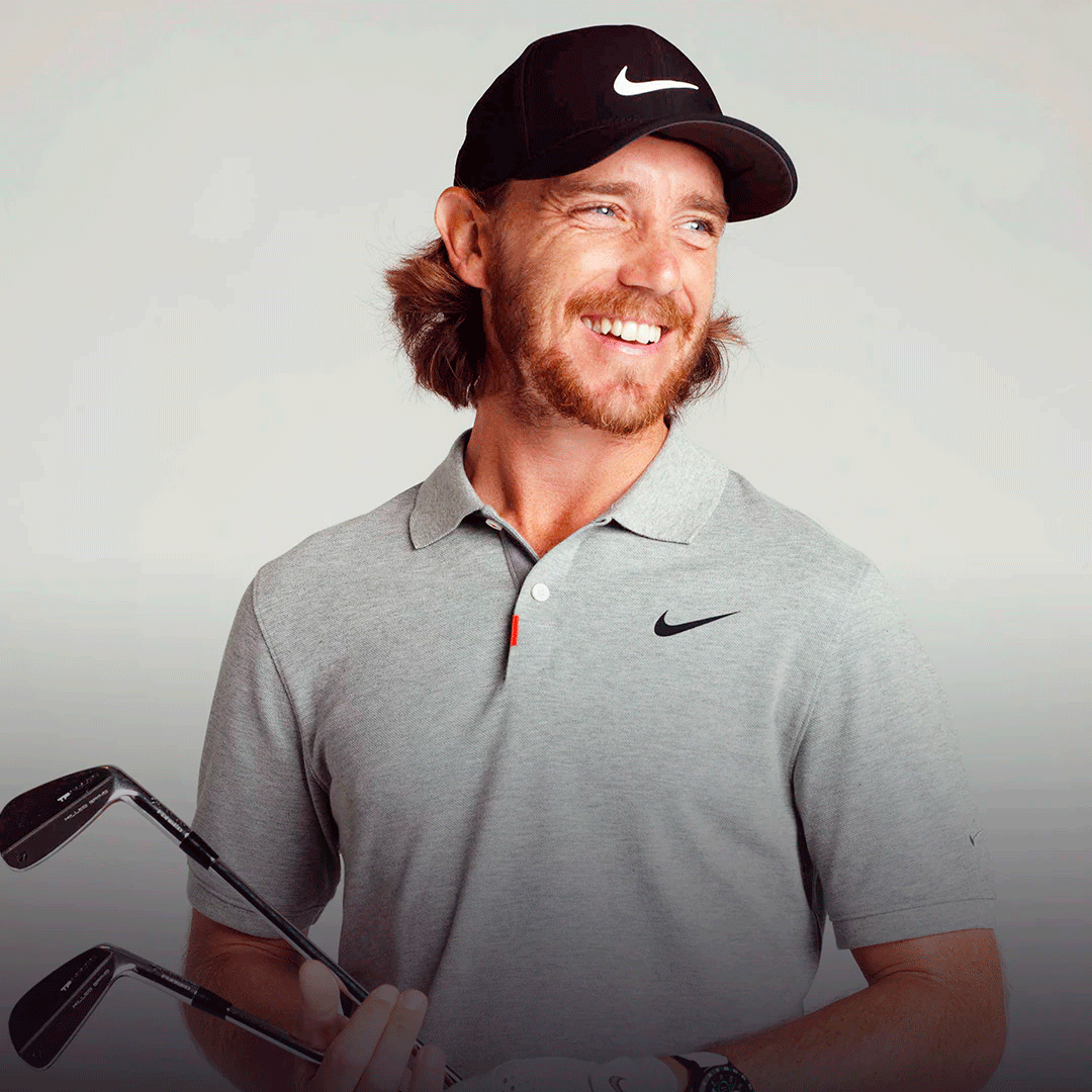 Professional golfer Tommy Fleetwood holding two golf clubs and smiling